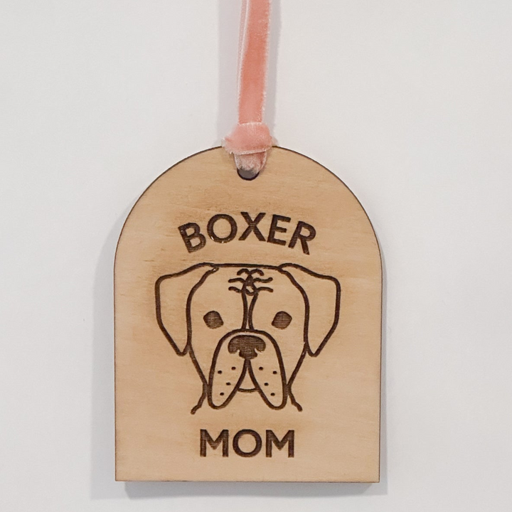 A wooden arch-shaped gift tag or ornament with a peach ribbon loop, featuring a laser-engraved illustration of a boxer dog and the words &