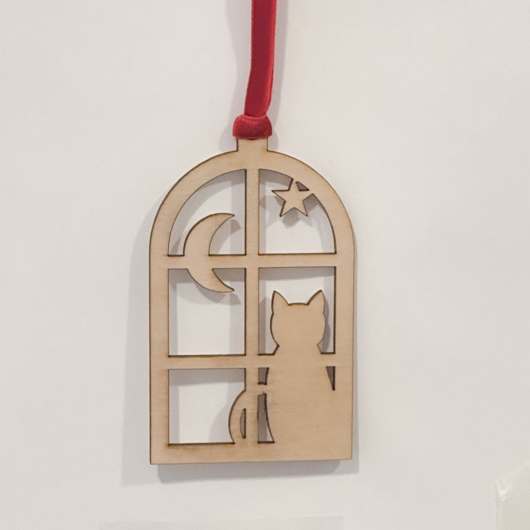 A wooden window-shaped hanging ornament with a red hanging ribbon, featuring a cat silhouette, crescent moon, and star cutouts, shown against a plain white background.