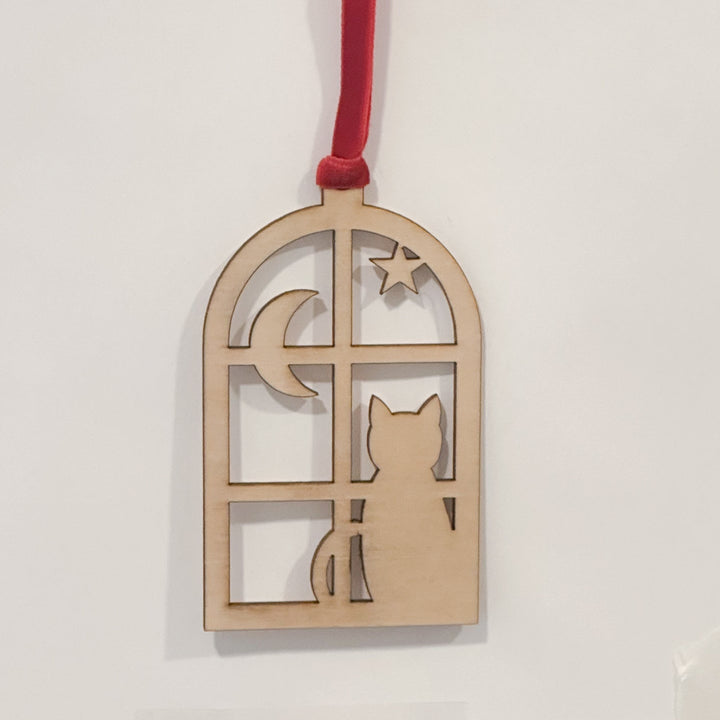 A wooden window-shaped hanging ornament with a red hanging ribbon, featuring a cat silhouette, crescent moon, and star cutouts, shown against a plain white background.