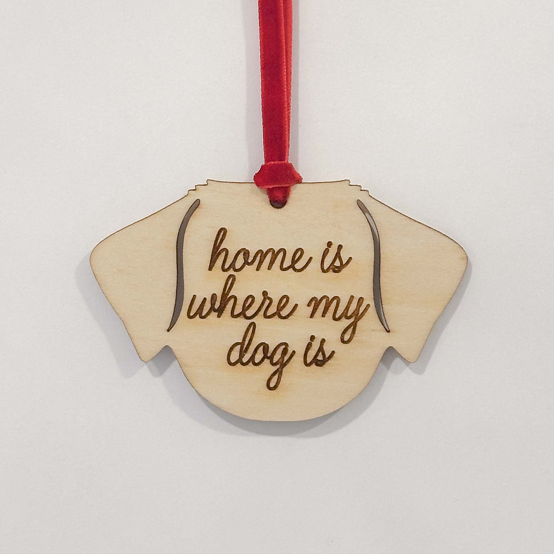 A wooden dog-shaped ornament with the engraved text 'home is where my dog is' and a red hanging ribbon, shown against a plain light background.
