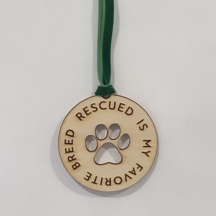 A round wooden pet memorial ornament with a green velvet hanging ribbon. The ornament is light natural wood with dark brown engraved text reading &